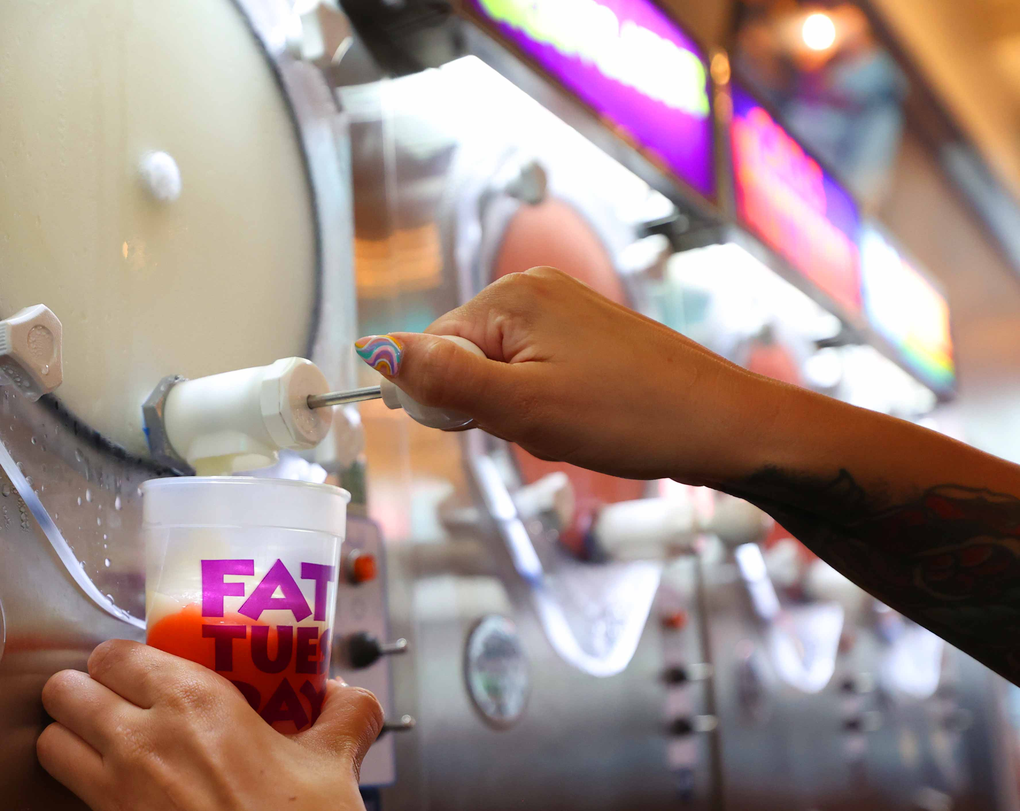 Someone filling a cup with a frozen drink from the tap on a massive chiller